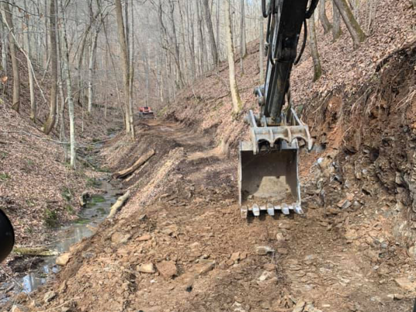 View of road construction in the woods from inside the backhoe. You can see the skidloader in the background.