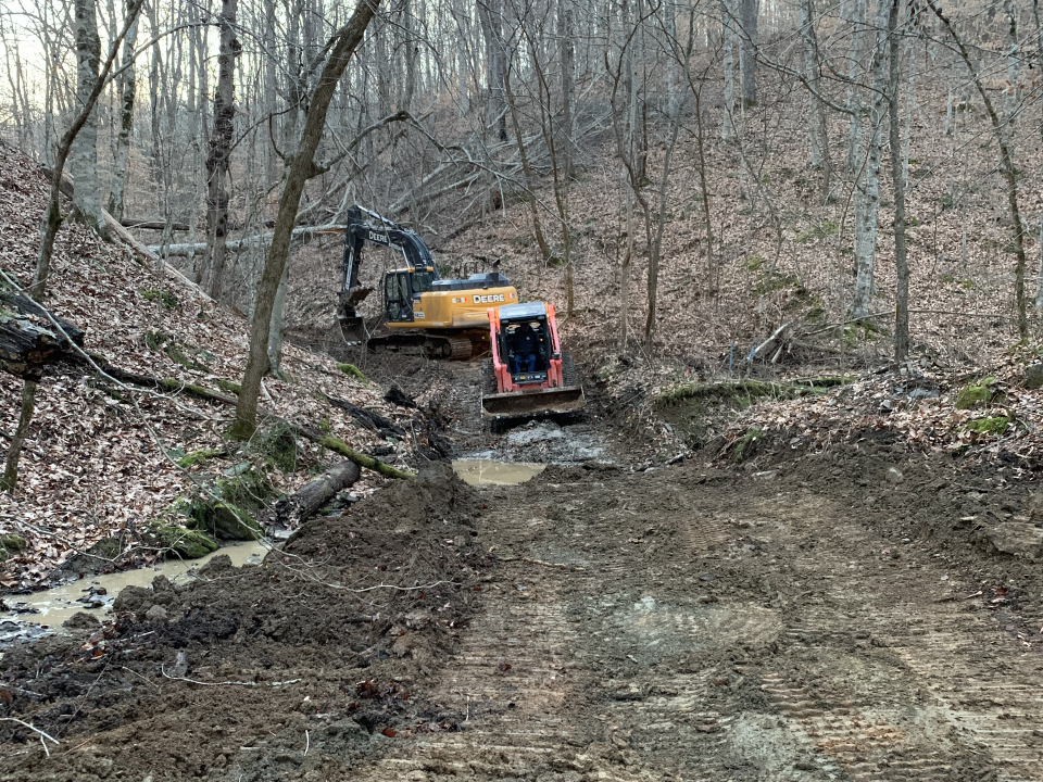 Road under construction through the woods using a backhoe.